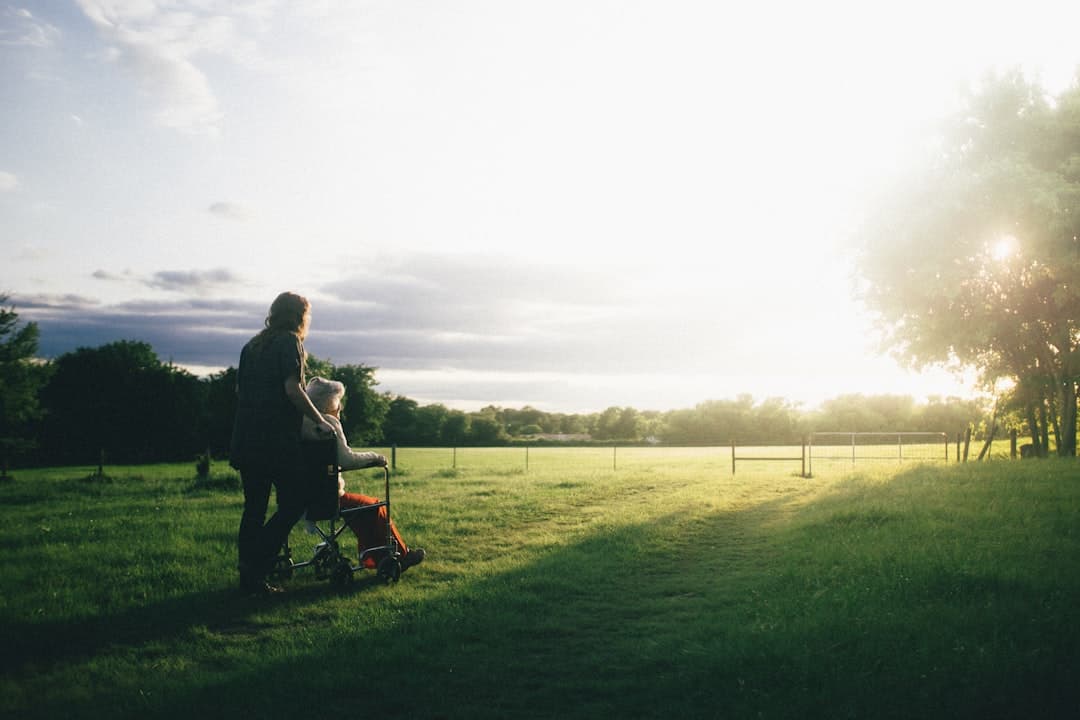 A woman pushing someone in a wheelchair across a field