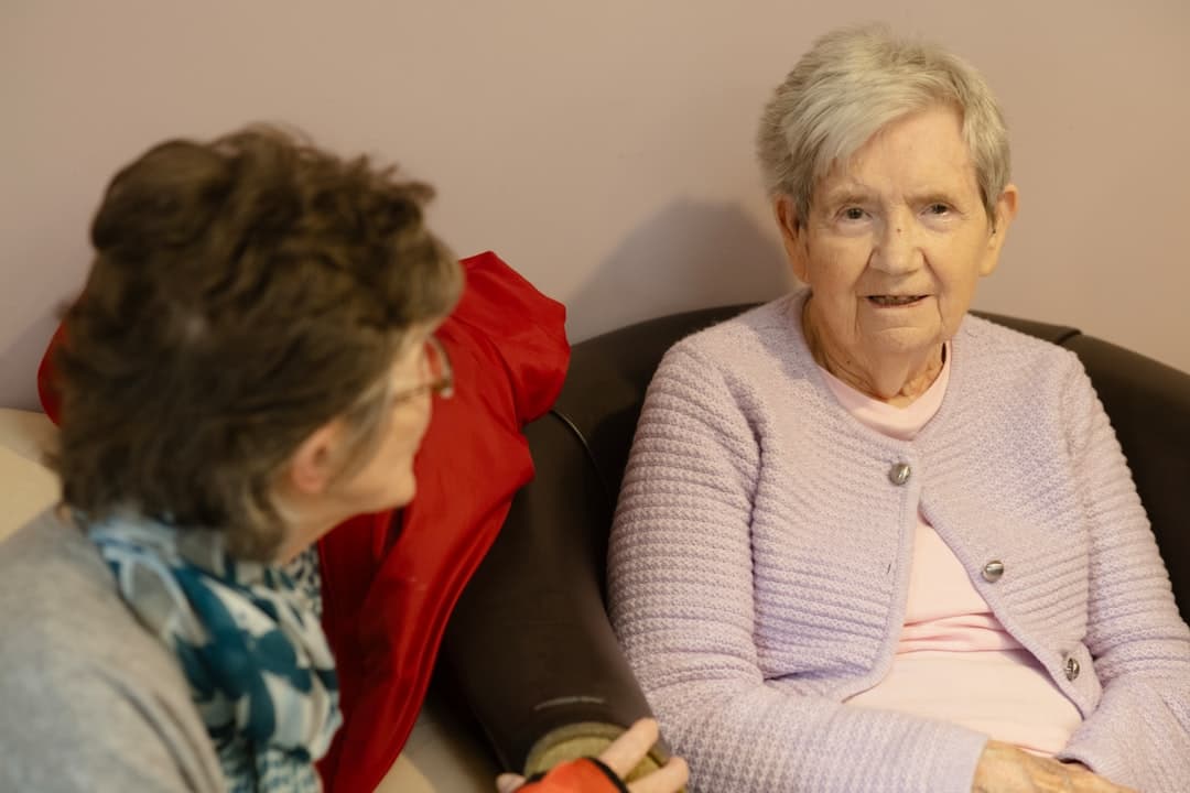 Two older women talking together on a sofa